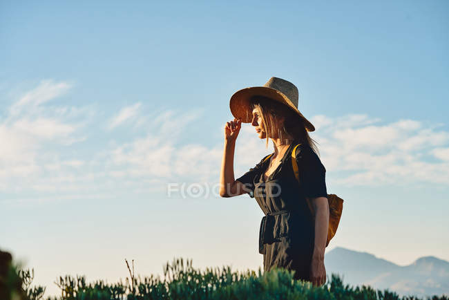 Turista donna che indossa cappello di paglia e zaino in piedi in natura — Foto stock