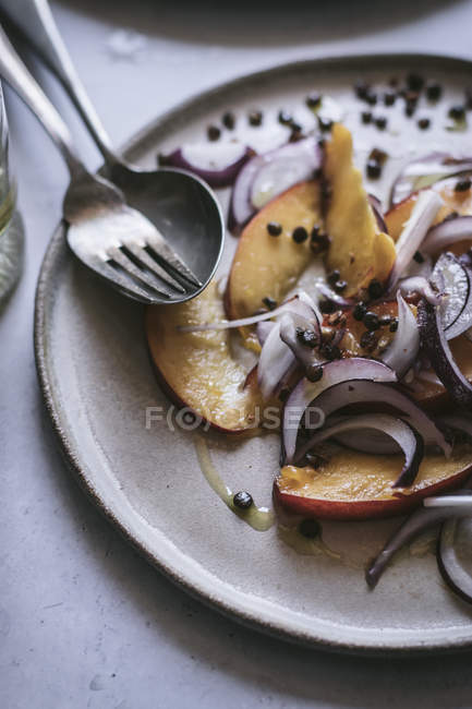 Placa con ensalada gourmet hecha de duraznos, cebolla roja, aceite y pimienta negra en la mesa - foto de stock