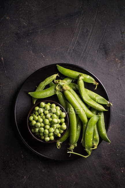 Peeled fresh peas and pea pods on dark wooden table — Stock Photo