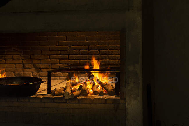 Orange flames of fire and black skillet on brick fireplace indoors — Stock Photo