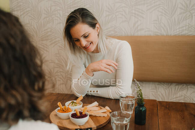 Attraktive junge Frau isst mit Freundin zu Mittag und verkostet appetitlichen Imbiss am Tisch — Stockfoto