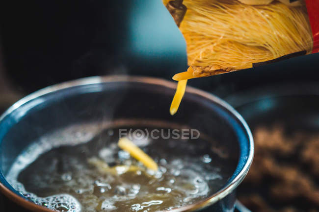Closeup raw pasta spill from box into saucepan with boiling water during food preparation in kitchen. — Photo de stock