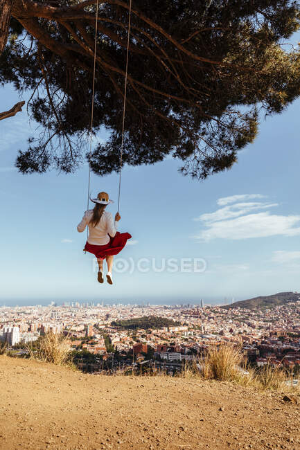 Дівчина розважається з червоною спідницею і капелюхом, розмірковуючи про місто на задньому плані — стокове фото