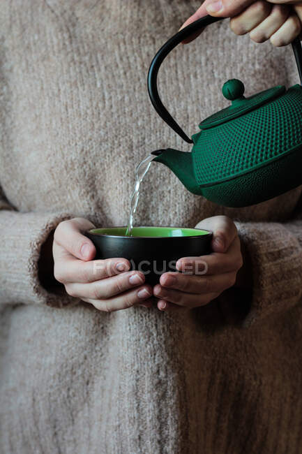 Personne versant le thé à la tasse dans les mains de la femme — Photo de stock