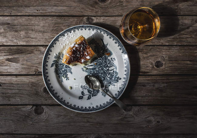 Vue de dessus de tranche de fromage cottage au four pudding servi sur assiette et verre de cognac sur table en bois — Photo de stock