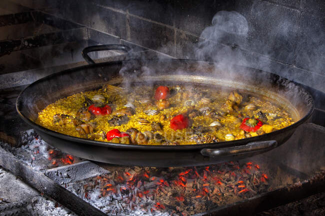 Paella deliciosa quente com arroz, frango e legumes cozidos em panela de ferro sobre fogo aberto — Fotografia de Stock