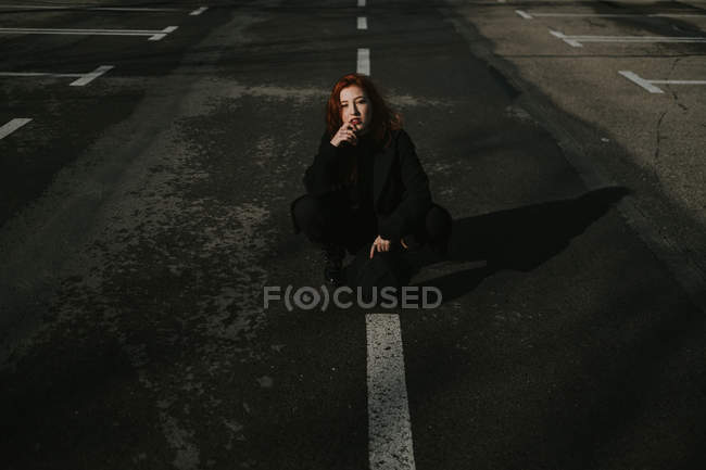 Mulher sorridente sentada na estrada com marcas brancas — Fotografia de Stock