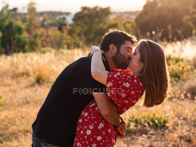 Man kissing smiling pregnant wife on background of picturesque green nature in sunny day — Stock Photo