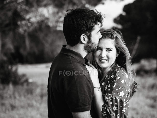 Мужчина обнимает улыбающуюся жену на фоне природы — стоковое фото