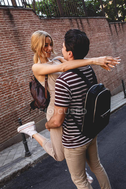 Cheerful young man having fun and carrying girlfriend during city date — Stock Photo