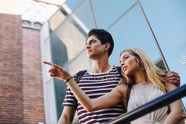 Attraente giovane coppia di turisti ammirando vista e puntando mentre in piedi di fronte a un edificio moderno — Foto stock