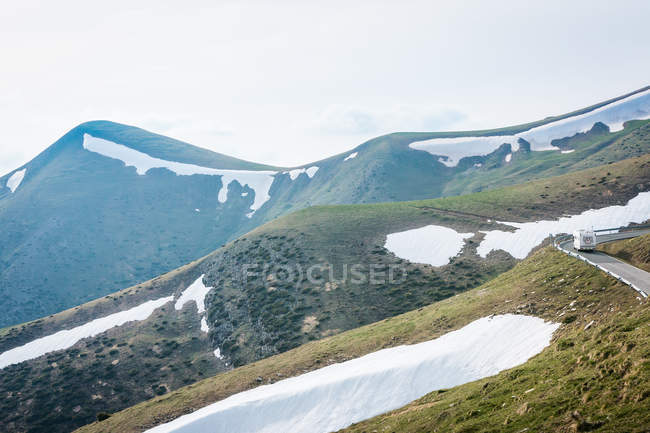 Camper blanc le long d'une route asphaltée sur une colline enneigée pendant une excursion en campagne alpine — Photo de stock