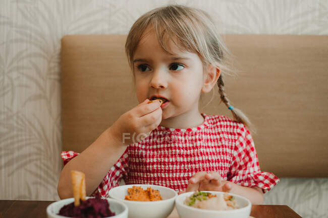 Linda niña comiendo surtido degustación aperitivo apetitoso en la mesa - foto de stock