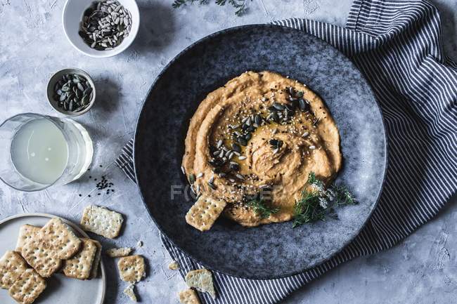Top view of cracker in plate with carrot and chickpea hummus decorated with seeds — Stock Photo