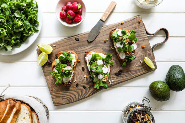 From above toasts with assorted vegetables placed on wooden cutting board on white tabletop — Stock Photo