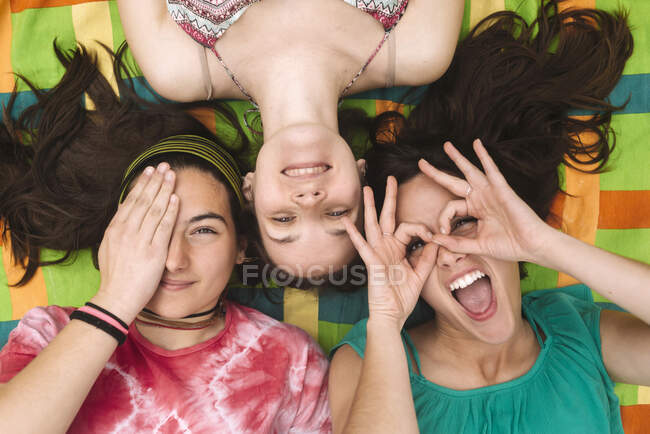 Desde arriba, las mujeres adolescentes jóvenes con ropa brillante se divierten y hacen caras mientras se tumban en coloridos cuadros - foto de stock