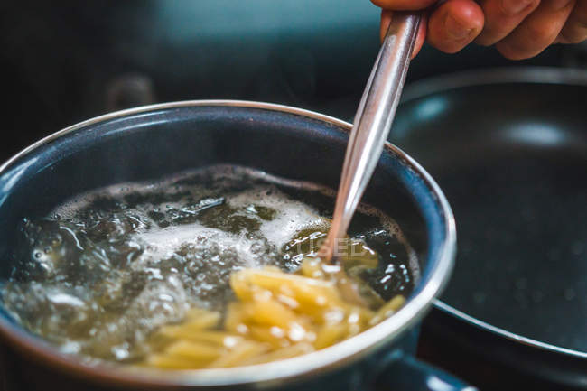 Nahaufnahme von Ernte unkenntlich Hand Kochen rohe Pasta verschüttet aus Box in Topf mit kochendem Wasser während der Zubereitung von Lebensmitteln in der Küche — Stockfoto