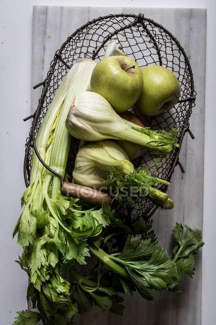 Von oben Metallkorb mit Äpfeln, Sellerie und Fenchelzwiebeln auf weißem Hintergrund — Stockfoto