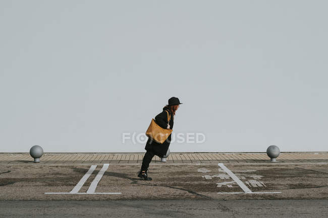 Seitenansicht einer stilvollen Frau in schwarzer Kleidung, die sich nach vorne beugt und auf der Straße gegen eine weiße Wand balanciert — Stockfoto
