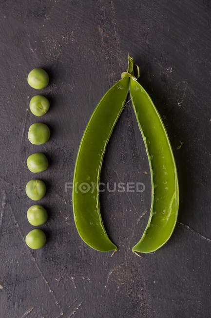 Peeled fresh peas in a row and pea pod on dark background — Stock Photo