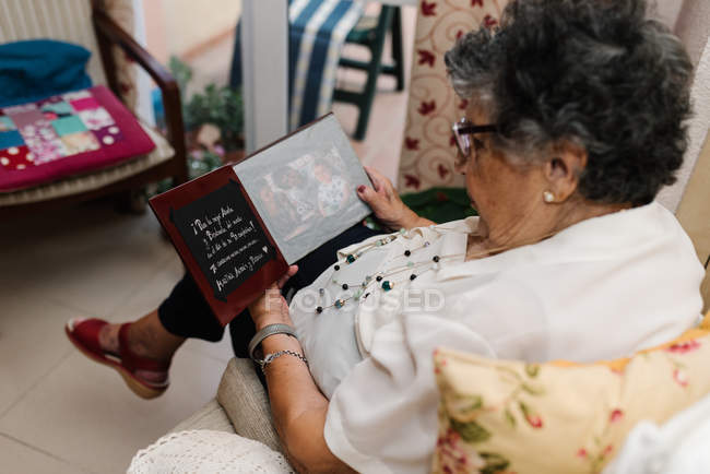 Senior woman in glasses looking at photo of granddaughter in album at home — Stock Photo