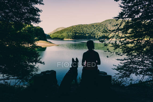 Woman with dog resting against beautiful lake — Stock Photo