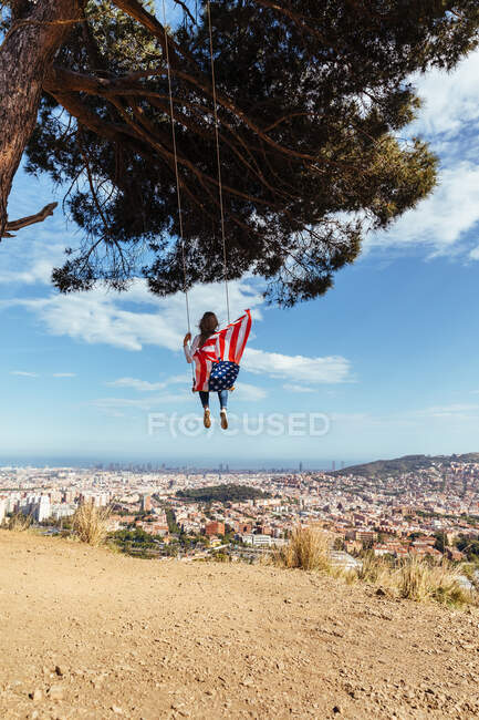 Junges Mädchen feiert den 4. Juli mit der amerikanischen Flagge auf einer Schaukel — Stockfoto