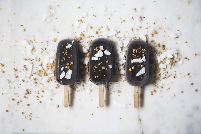 Assorted chocolate ice cream popsicles covered with toppings on marble surface — Stock Photo