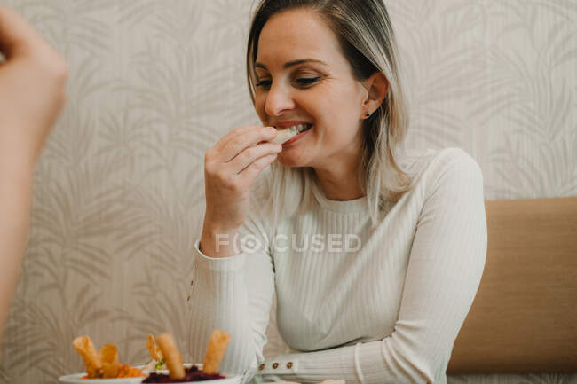 Attractive young woman having lunch with friend and tasting appetizing snack at table — Stock Photo