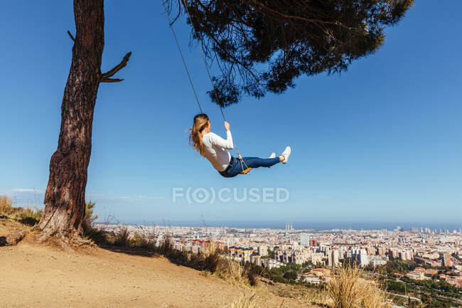Blonde girl swinging with city view in background — Stock Photo