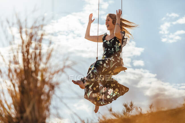 Щаслива дівчина з сукнею насолоджується гойдалкою на заході сонця — стокове фото