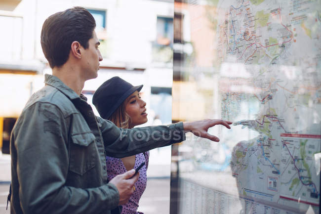 Young attractive couple of tourists looking at map in street — Stock Photo