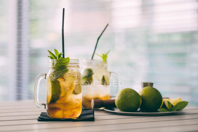 Two mojito cocktails prepared with lime, mint, rum, soda and ice in mason jars on table — Stock Photo