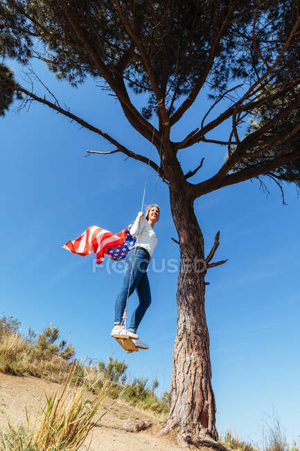 Menina comemorando o 4 de julho com a bandeira americana em um balanço — Fotografia de Stock