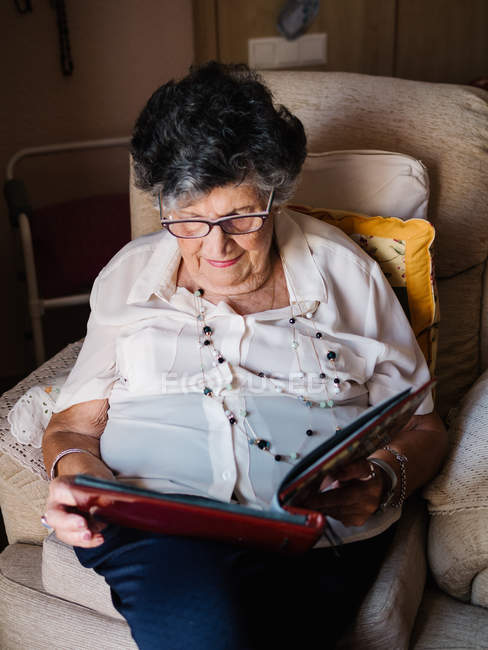 Старша жінка в окулярах дивиться на фотографії в альбомі вдома — стокове фото