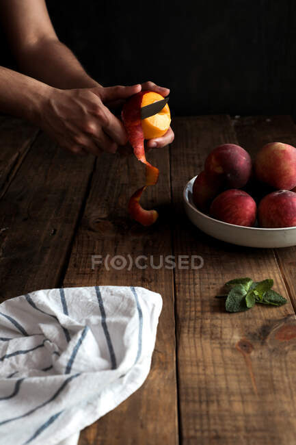 Tasty ripe peaches in plate and hands peeling peach — Stock Photo