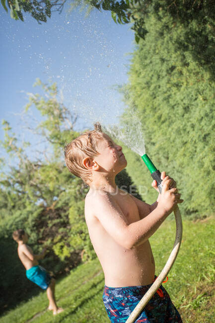 Малыш в купальниках брызгает водой из садового шланга на себя — стоковое фото
