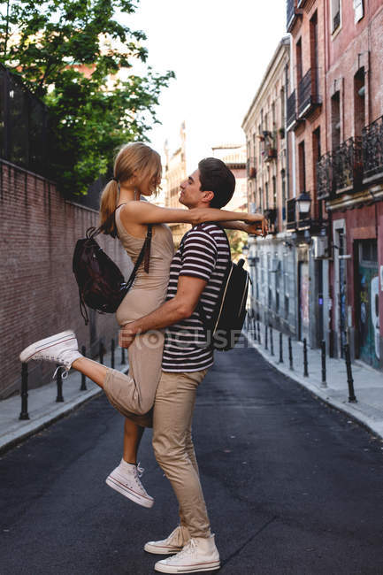 Cheerful young man having fun and carrying girlfriend during city date — Stock Photo
