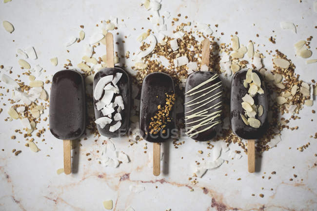 Assorted chocolate ice cream popsicles covered with toppings on marble surface — Stock Photo