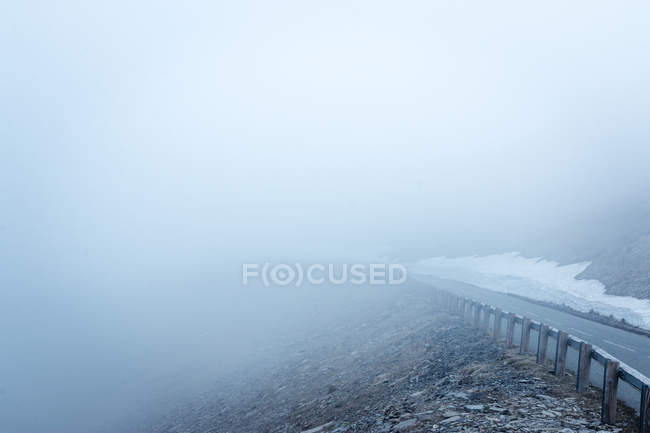 Strada asfaltata stretta che va sul pendio di montagna attraverso nebbia spessa nella natura — Foto stock