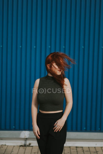 Redhead woman squinting in sunlight and enjoying weather against blue wall — Stock Photo