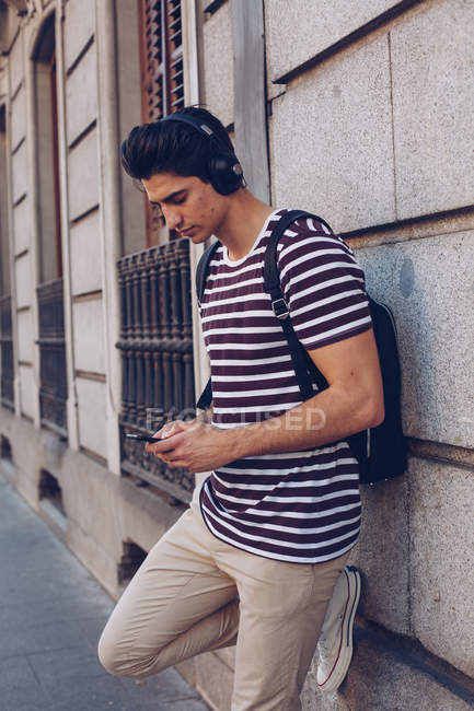 Attraente giovane uomo in abiti casual ascoltare musica durante la passeggiata in strada alla luce del giorno — Foto stock