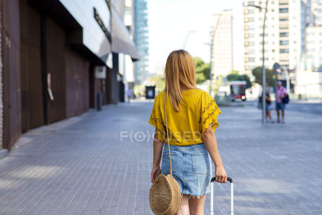 Vista posteriore di giovane turista donna con valigia che cammina per strada — Foto stock