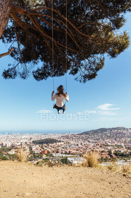 Blonde girl swinging with city view in background — Stock Photo