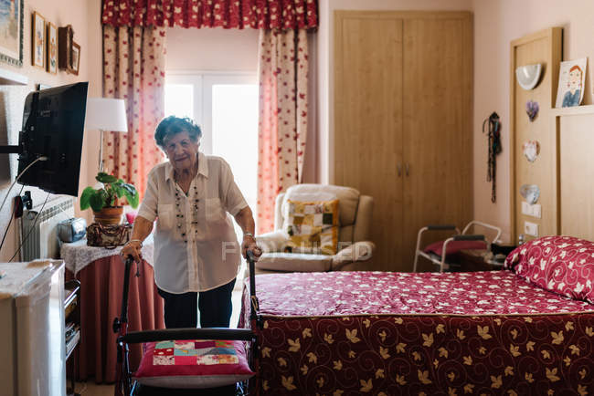 Femme âgée en chemisier avec marcheur dans la chambre et regardant la caméra — Photo de stock
