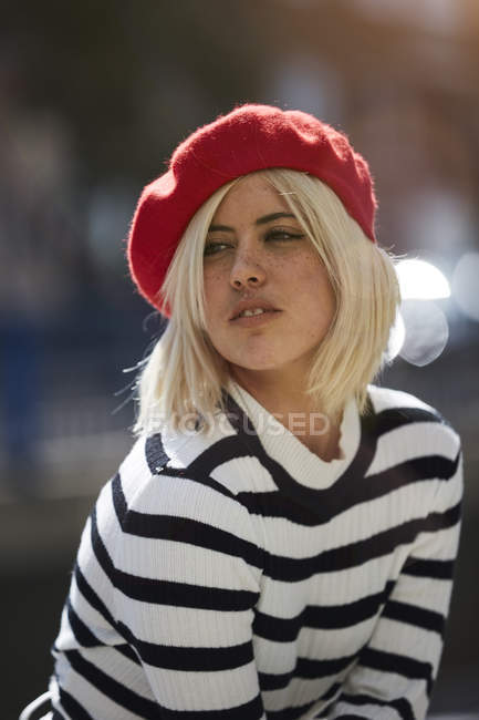 Young blonde woman in striped black and white shirt and red French cap on blurred background — Stock Photo