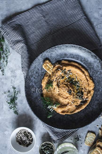 Vue du dessus du craquelin dans une assiette avec carotte et houmous de pois chiches décorés de graines — Photo de stock
