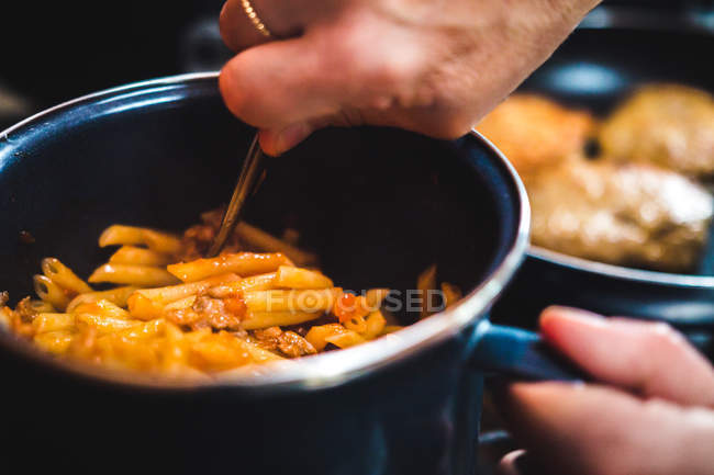 Closeup of crop unrecognizable hand cooking pasta in a saucepan with meat in kitchen — Stock Photo