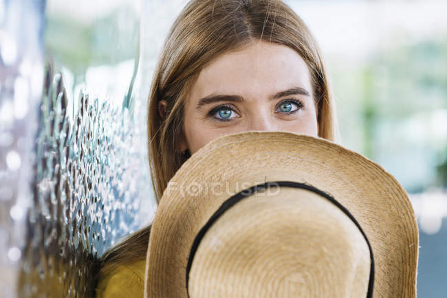 Young blonde woman with blue eyes covering face with straw hat — Stock Photo