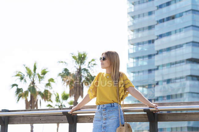 Jovem mulher em saia jeans e camiseta amarela em pé na ponte e olhando para longe — Fotografia de Stock